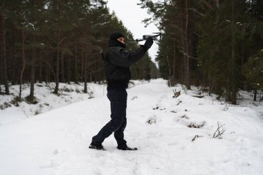 Siyah elbiseli bir erkek sınır muhafızı kış ormanında elinden drone fırlatıyor.. 