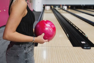 Bowling oynayan bir kız, yüzü olmayan yakın plan bir fotoğraf, elinde kırmızı bir bowling topu. 
