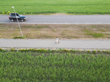 Küçük bir kız yaya yolunda scooter kullanıyor ve yakınlarda bir otoyolda bir araba sürüyor. Bir İHA 'dan fotoğraf görüntüsü. 
