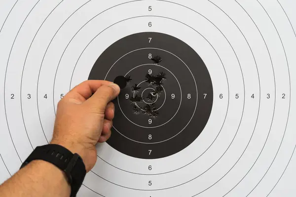 Atış poligonunda kağıttan bir hedefe ateş etmek, bir adamın eli hedefteki kurşun deliklerini kapatır.. 