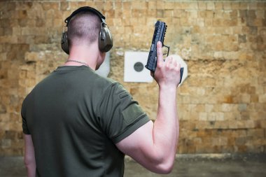 Elinde tabanca olan atletik bir adam atış poligonunda antrenman yapıyor.. 