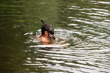Erkek bir su altı avcısı bir yaz günü şnorkel ve maskeyle nehirde yüzer.. 