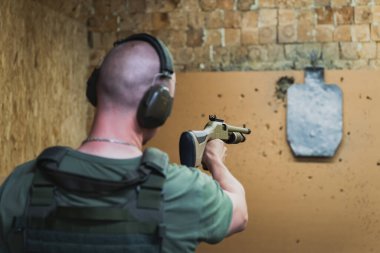 Plaka taşıyıcıdaki bir erkek nişancı atış poligonundaki metal bir hedefe nişan alır.. 