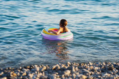 Sahilde tehlike var. Küçük bir kız çocuğu bir yaz günü plajda şişme bir oyuncak üzerinde yüzer..