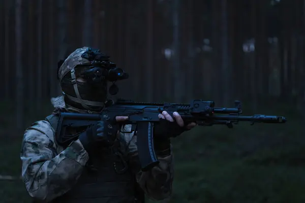 stock image Military special forces with a night vision device in a balaclava with a machine gun with a laser sight at dusk in the forest.