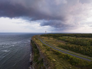 Paldiski peninsula, road near the cliff leading to the lighthouse, stormy sky and waves in the sea, photo view from a drone at sunrise. clipart