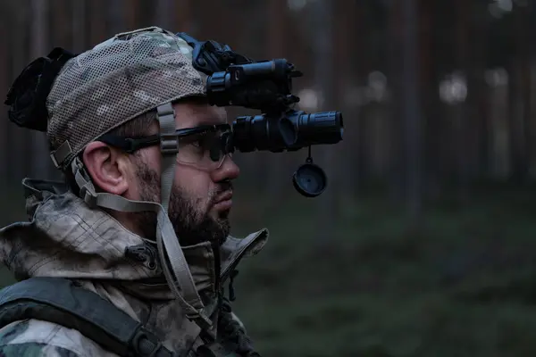 Avrupalı bir asker kamuflajlı ve kafasında gece görüş cihazıyla ormanın ortasında alacakaranlıkta. Yakın plan fotoğraf.. 