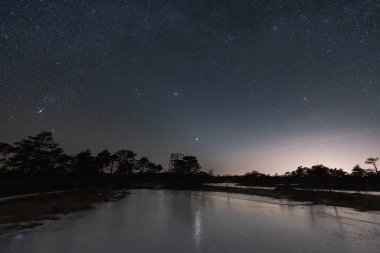 Night landscape astrophotography in the nature of Estonia in winter. Frozen Seli bog, observation tower and starry sky. clipart