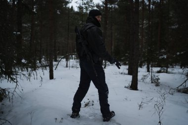 Sırtında tüfek, elinde tabanca olan özel bir asker. Kış ormanında, alacakaranlıkta. Fotoğraf arkadan.. 