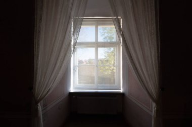 Parlak bir avluya bakan karanlık eski bir evin penceresi. Perili bir ev. 