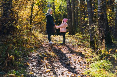 Young mother with her 7 year old daughter in the forest during leaf fall on an autumn day. Nature of Latvia. clipart