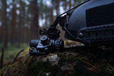 Gece görüş cihazı taktik bir kaska monte edilmiş. Ormanda yok edilmiş bir sığınağın yanında çekilmiş bir fotoğraf..