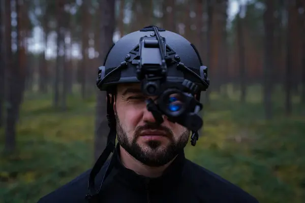 Karanlık bir ormanda gece görüşü cihazıyla taktik kasklı sakallı bir adam..