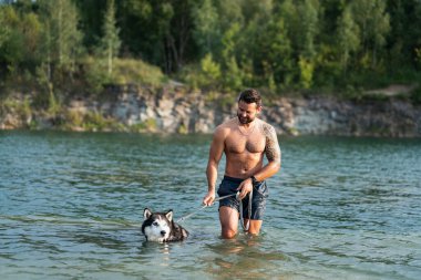 Bir erkek köpek sahibi Sibirya köpeğiyle yaz günü mavi bir su gölünde parti yapıyor. Rummu Taş Ocağı.