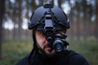 Karanlık bir ormanda gece görüşü cihazıyla taktik kasklı sakallı bir adam. Yumuşak odaklı fotoğraf. 