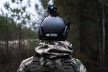 Gece karanlığında ormanda miğferli bir askeri eğitmen ve gece görüş cihazı. Arkadan bak..