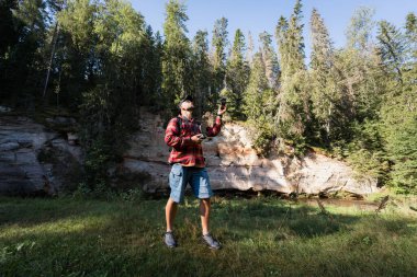 A male landscape photographer launches a drone in the nature in the forest on a summer day. clipart