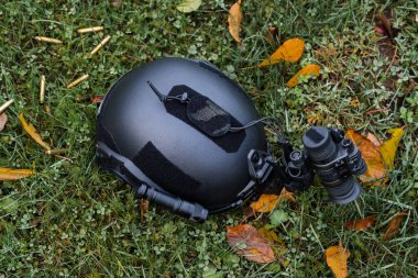 Black military ballistic helmet with night vision device and flashlight lies on the ground, tactical gear.