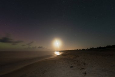 Kuzey Işıkları, ay ve yıldızlı gökyüzü Baltık Denizi ve kumlu sahil Perakula geceleri.