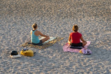 İki orta yaşlı kadın yaz sabahı Nice plajında yoga yapıyor.. 