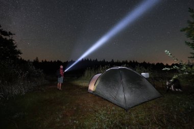 Sonbaharda göl kenarındaki çadırda yıldızlı gökyüzü olan vahşi bir gece kampı. Yanında feneri olan bir adam duruyor..