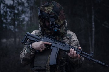 Tüfekli bir asker ve karanlık çöktüğünde ormanda gece görüşlü bir miğfer..