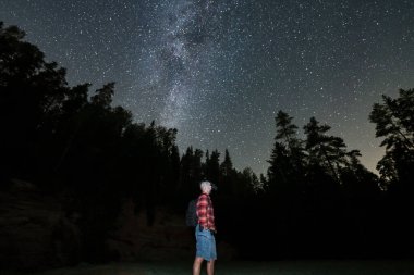 Night hiking, man with night vision goggles on his head in night forest with starry sky. clipart