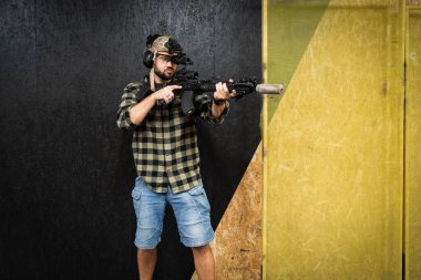 Sivil giysili bir adam gece görüşü monoküler ve atış poligonunda susturuculu bir tüfekle taktik atış talimi yapıyor..