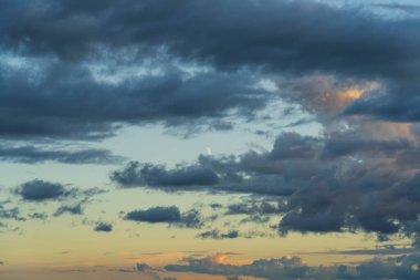 Crescent moon peeking through clouds at sunset.  clipart