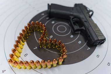 A pistol and bullets arranged in the shape of a heart on a shooting target. A conceptual photo symbolizing love and danger, passion and aggression. clipart