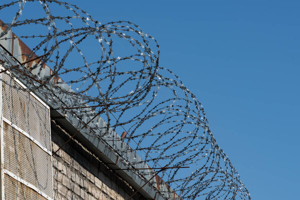 Prison walls with barbed wire against a blue sky. Concept of imprisonment, deprivation of liberty.
