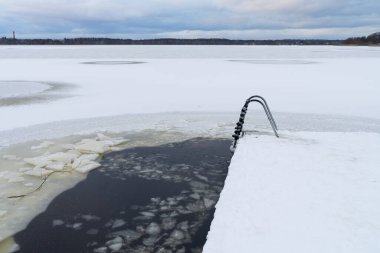 Ladder to the ice hole on a frozen lake. Winter swimming in icy water. Harku lake. clipart