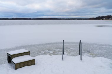 Kışın yüzmek için buz çukuruna bir merdiven. Sertleştirme, kış yüzme, sağlık, buzlu su aşırı, aktif yaşam tarzı, gelenekler. Estonya doğası.