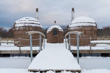 Winter relaxation: three cozy barrel saunas on a snowy lake. clipart