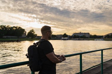 Güneş gözlüklü bir gezgin Krakow 'daki Vistula Nehri üzerinde günbatımının tadını çıkarıyor..
