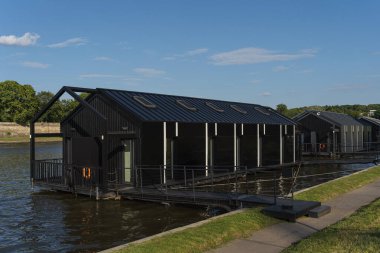 Güneşli bir günde Polonya 'nın Krakow kentindeki Vistula Nehri üzerinde terası olan modern siyah yüzen ev. Arka planda yeşil ağaçlar ve mavi gökyüzü görülebilir..