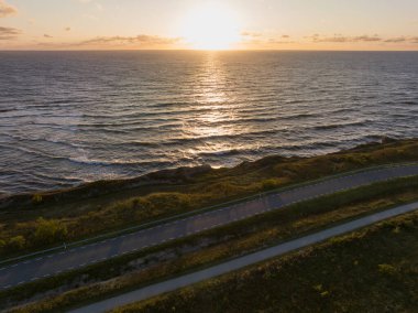 Paldiski, Estonia: Drone view of a winding coastal road receding into the horizon, next to the Baltic Sea, in the sunset light. clipart