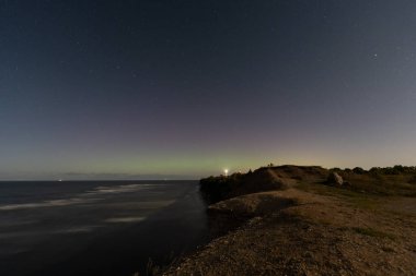 Night landscape: starry sky, lighthouse on a cliff, and calm sea. clipart