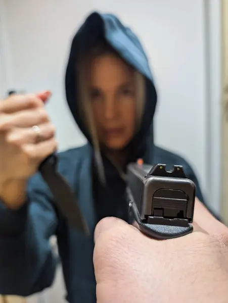 Kapüşonlu sarışın soyguncu kız elinde bıçakla iyi bir adama silah doğrulttu. Dikey fotoğraf.