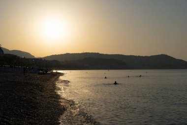 Altın gün batımı, alacakaranlıkta eriyen yüzücülerin gölgelerinin plajını sarar..