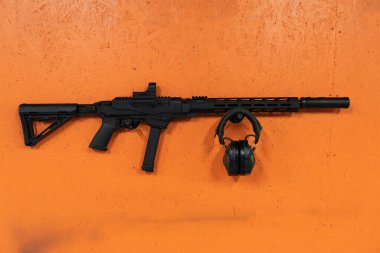 9mm 'lik susturuculu ve aktif kulaklıklı taktik tüfek turuncu bir duvarda asılı..