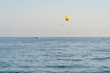 Parasailing açık denizde: parlak bir paraşüt bir tekne çeker, güneşli bir günde dalgaların üzerinde uçmaktan zevk alır.. 