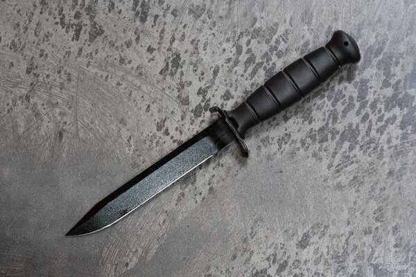 A sharp black army knife lies on the concrete floor.
