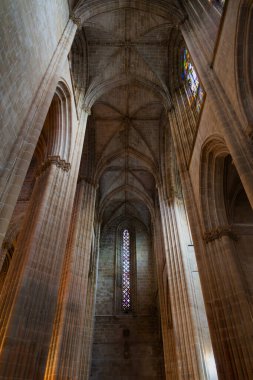Yükselen Gotik sütunlar, ışıkla yıkanmış vitray pencereler ve Lizbon Katedrali 'nin gizemli derinlikleri. Dikey fotoğraf.