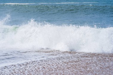 Köpüklü bir ibikli güçlü bir dalga kumlu bir sahile çarpar ve nefes kesici bir doğal güç gösterisi yaratır..