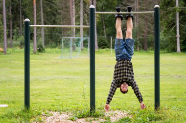 Yerçekimi botlu atletik bir adam bir yaz günü açık havada yatay bir barda asılı durur. Sağlıklı yaşam tarzı.