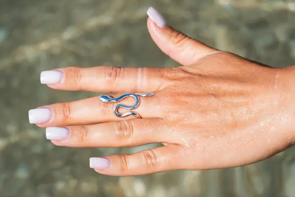 Bir kadının elinde zarif gümüş bir yılan yüzüğü, deniz kıyısında bir arka planda zarif bir manikür, zarif bir mücevher tasarımı..
