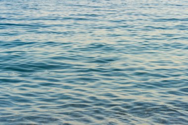 Şafak vakti sakin deniz yüzeyi, güneş ışığıyla oynayan yumuşak dalgalar, sakin bir atmosfer yaratıyor..