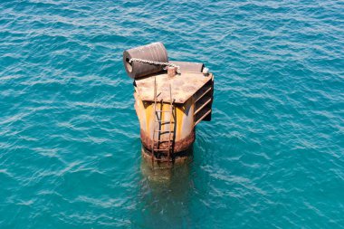 Açık okyanusta terk edilmiş metal şamandıra, kavurucu güneşin altında paslanıyor, bir merdiven ve zincirle..