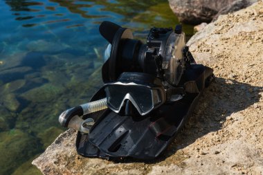 Dalış takımları ve kayalık bir göl kıyısındaki su altı evlerinde bir kamera..